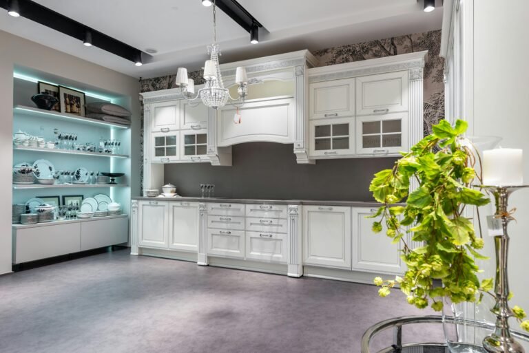 Interior of spacious kitchen with white wooden cupboard and shelves with illumination with kitchenware and glass table with green plant and candleholder